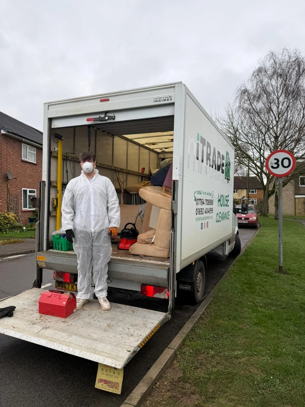 iTrade team member in protective coveralls beside an open vehicle containing household furniture
