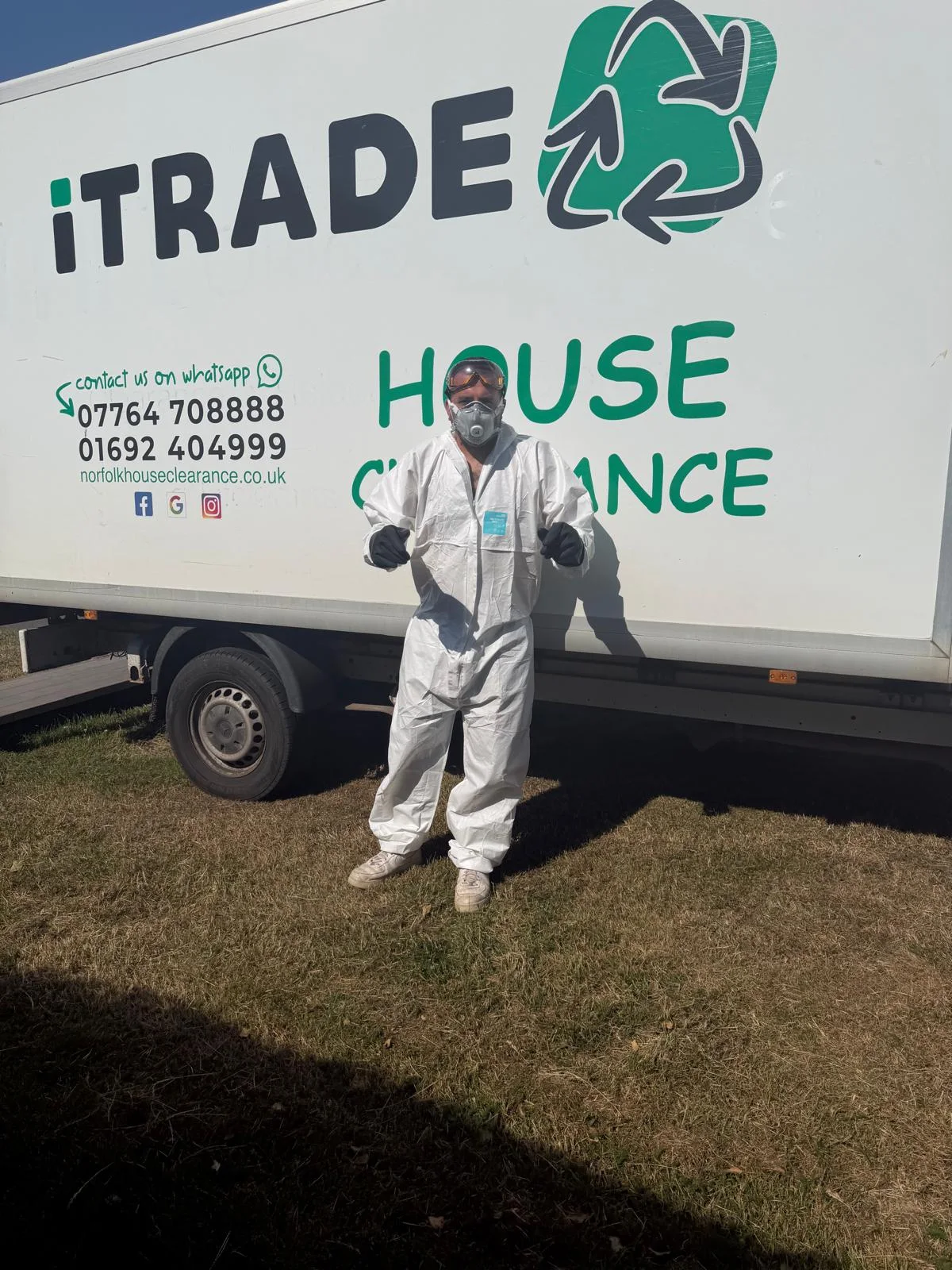 iTrade team member wearing protective coveralls, gloves, goggles and a respirator beside a branded vehicle